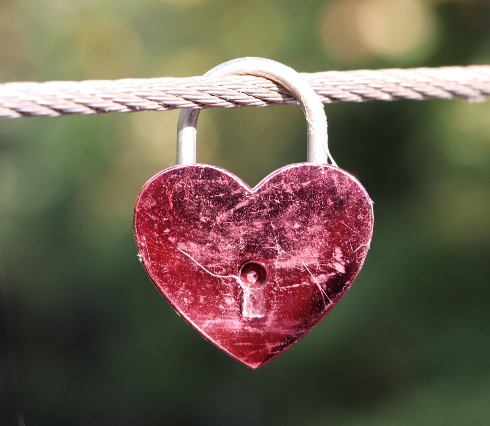 A red heart-shaped padlock hanging on a cable, symbolizing love and commitment.
